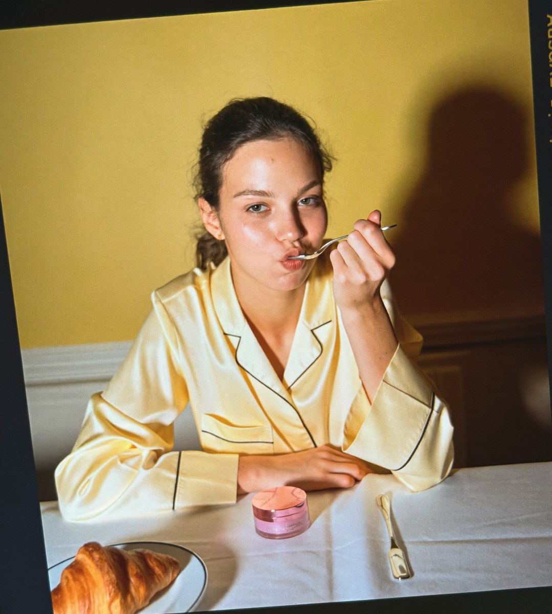 Une femme en pyjama de soie mange son pot de soin à la cuillère à dessert, croissant intact