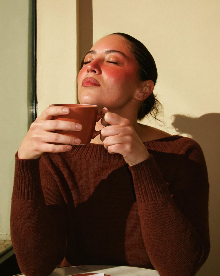 Une femme goûte son café les yeux fermés, lumière d'après-midi
